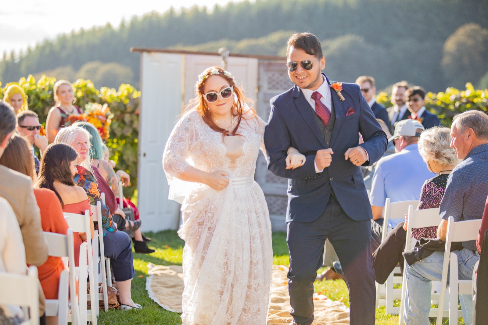 Bride and groom in sunglasses dance down the aisle past seated guests