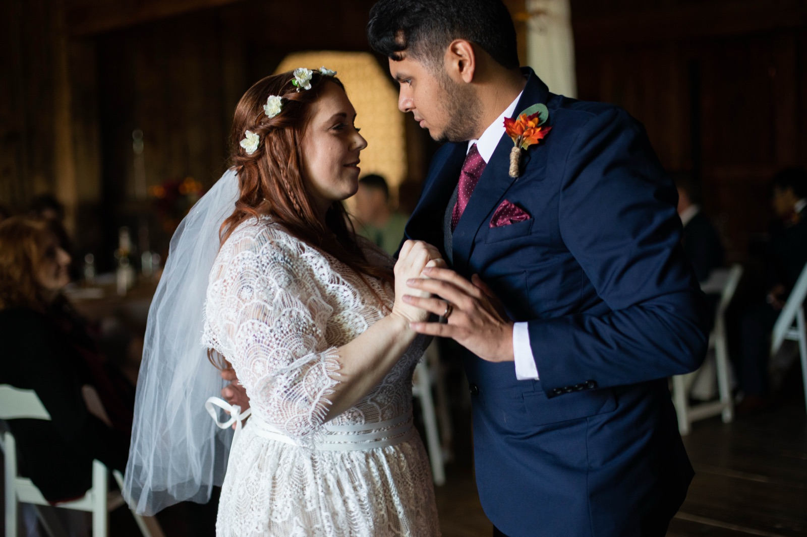Bride and groom hold hands close during their first dance in a wooden barn