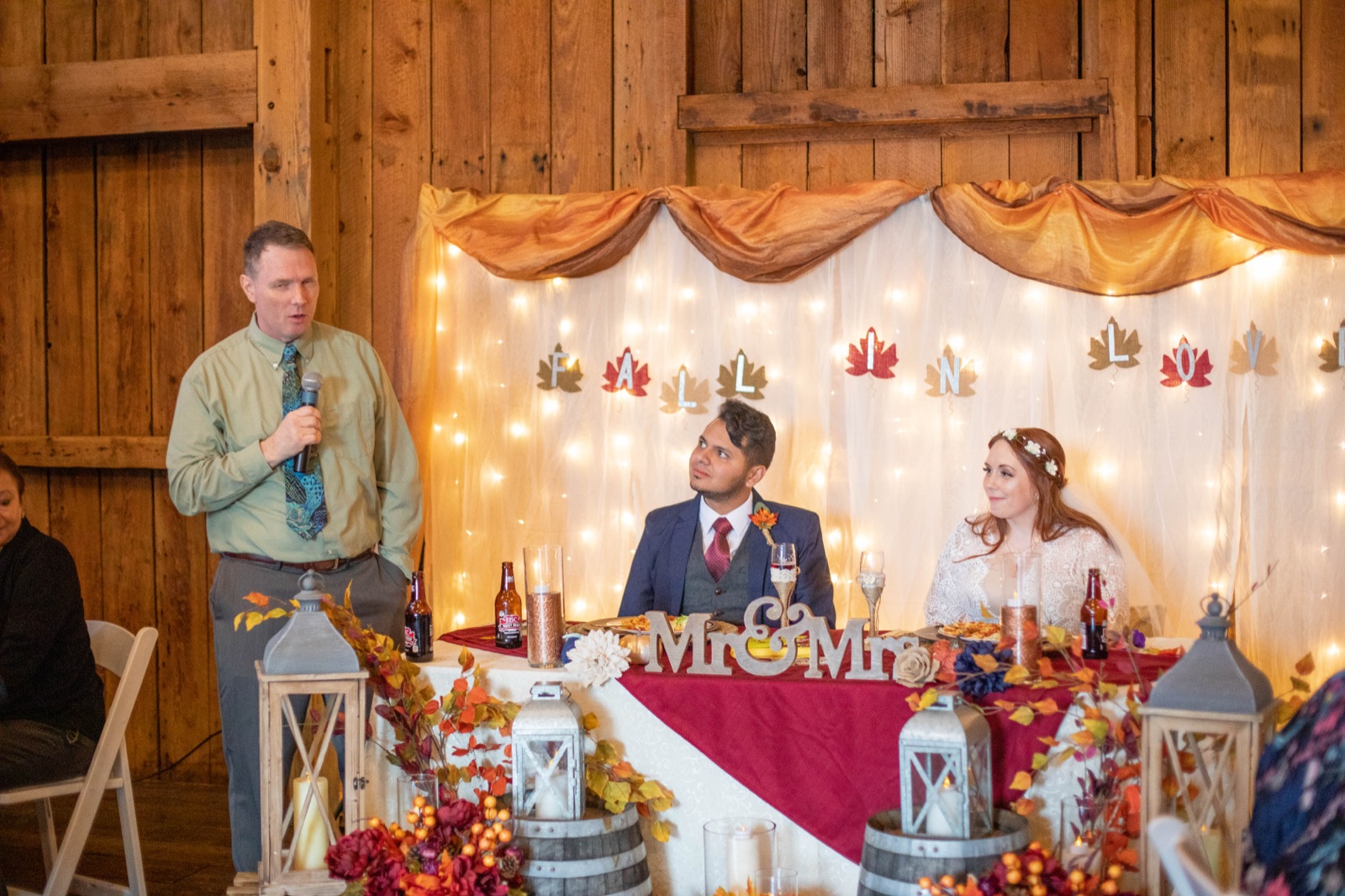 Bride and groom sit back to back playing the shoe game, each raising a shoe overhead in a barn reception