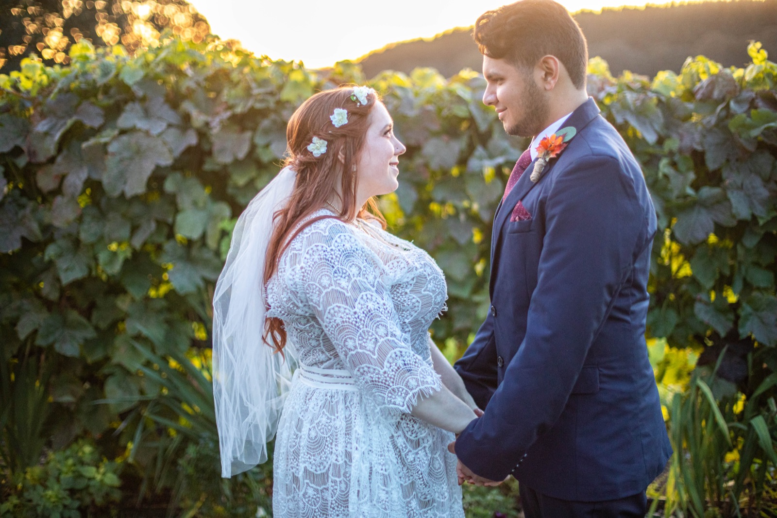 Bride and groom hold hands facing each other at golden hour beside a vineyard row