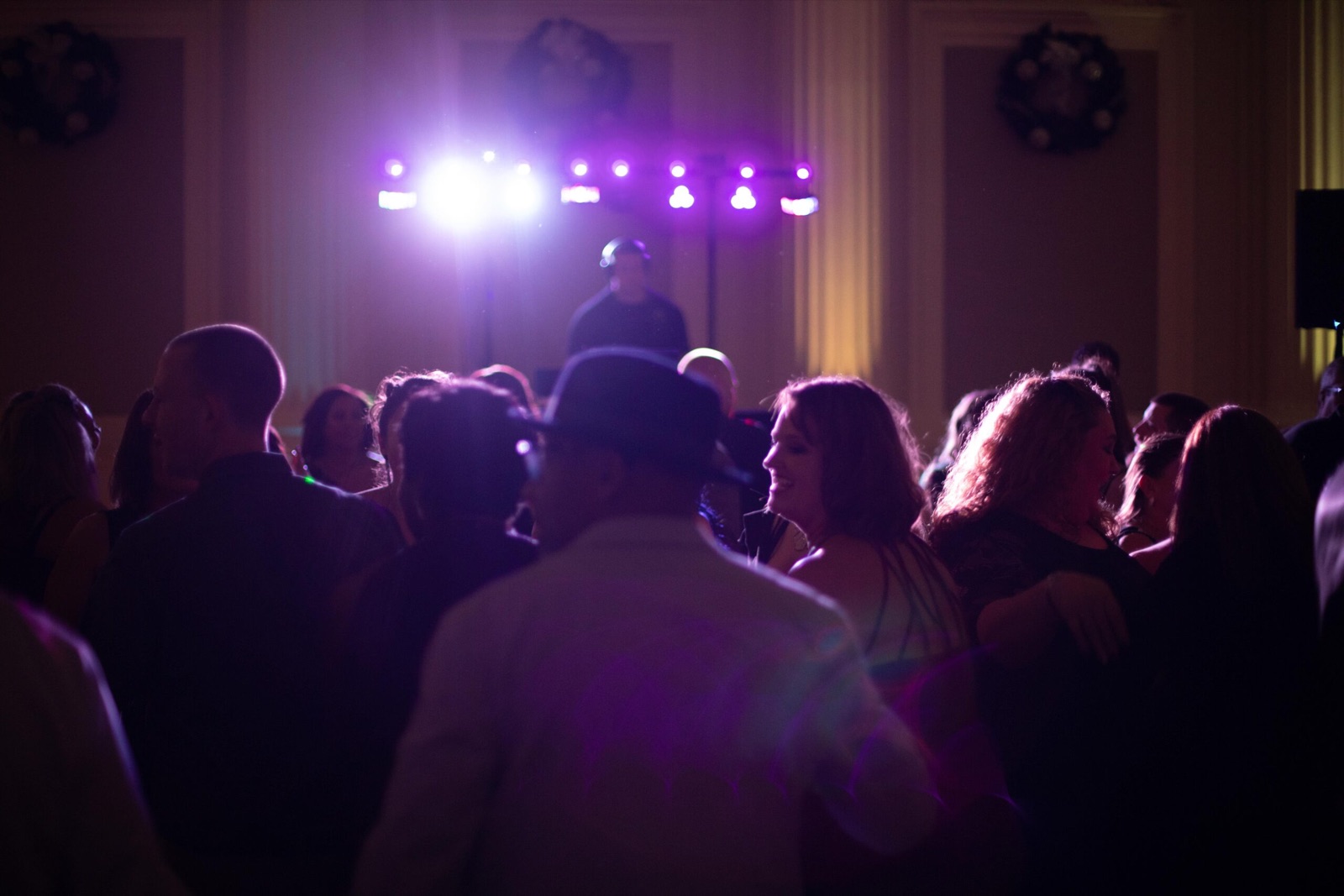 Guests fill a ballroom dance floor under purple lighting with the Apogee DJ at his booth