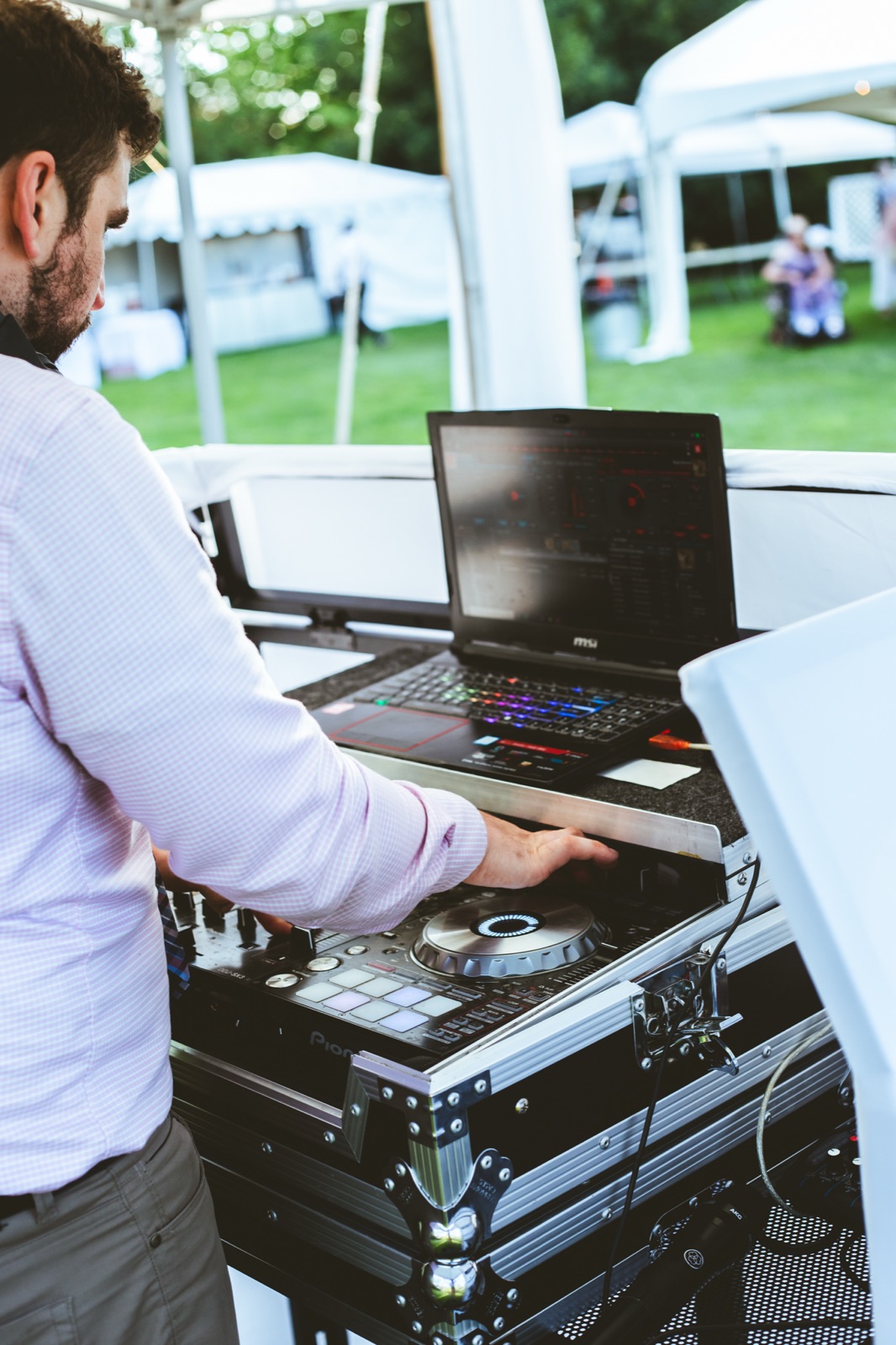 DJ Allen Carter mixes on a Pioneer controller and laptop under a white tent at an outdoor wedding in Bend