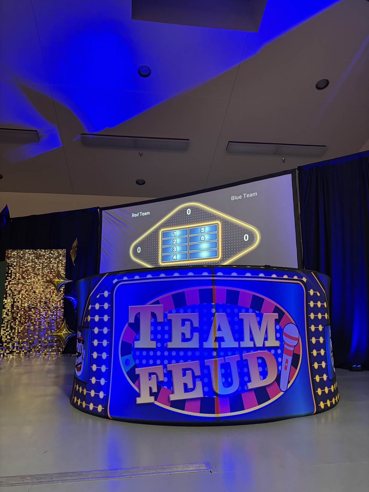 Team Feud LED game-show podium in front of a projected Red Team vs Blue Team survey board