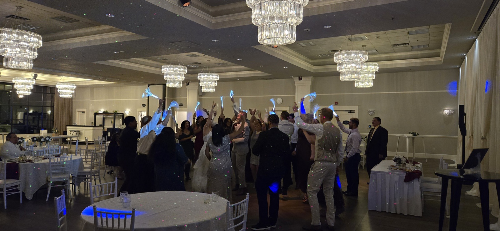 Wedding guests wave fiber-optic light wands on a ballroom dance floor under crystal chandeliers in Portland