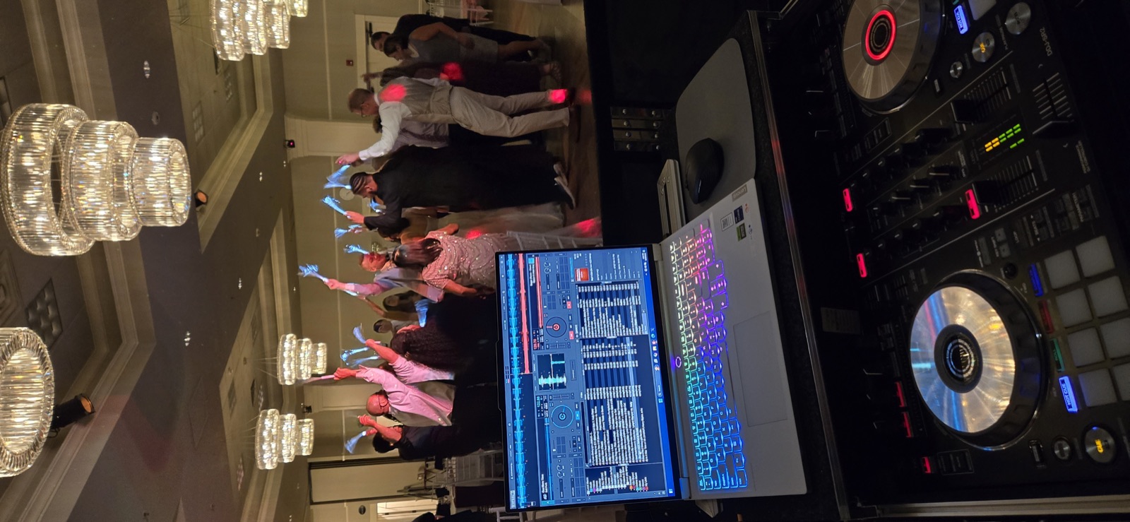 DJ controller and laptop in the foreground as wedding guests wave glow sticks under chandeliers in Portland, Oregon