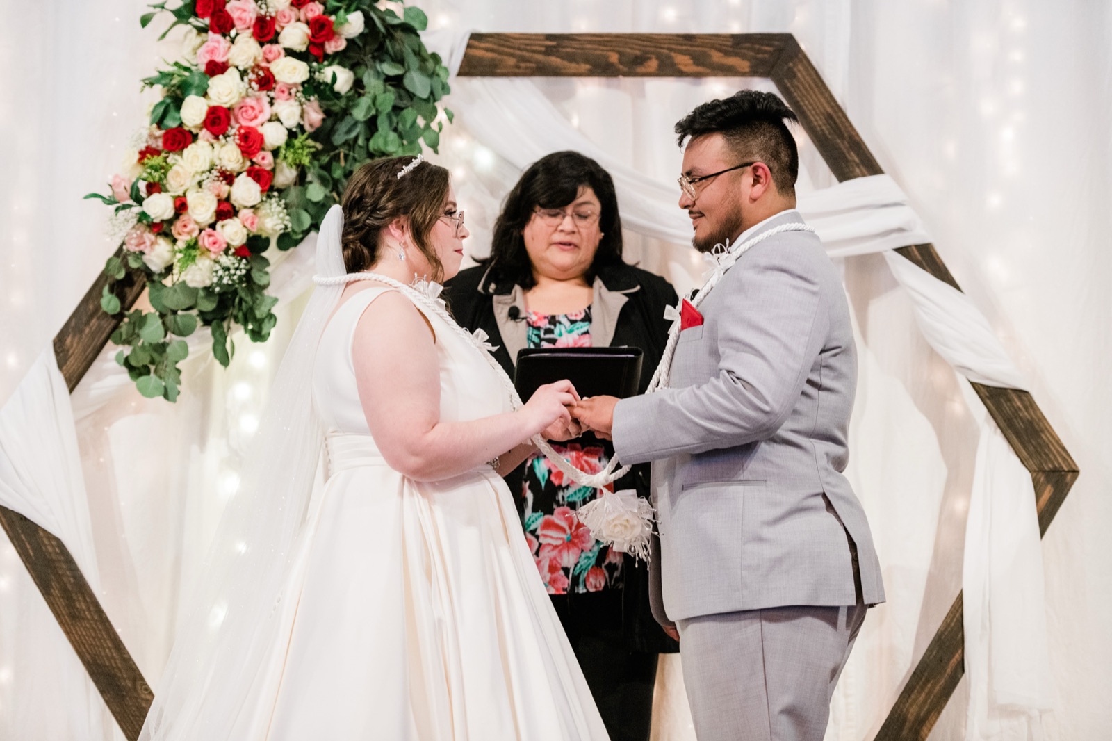 Bride and groom holding hands during the ceremony under a hexagon wood arch with roses at Green Villa Barn in Independence, Oregon