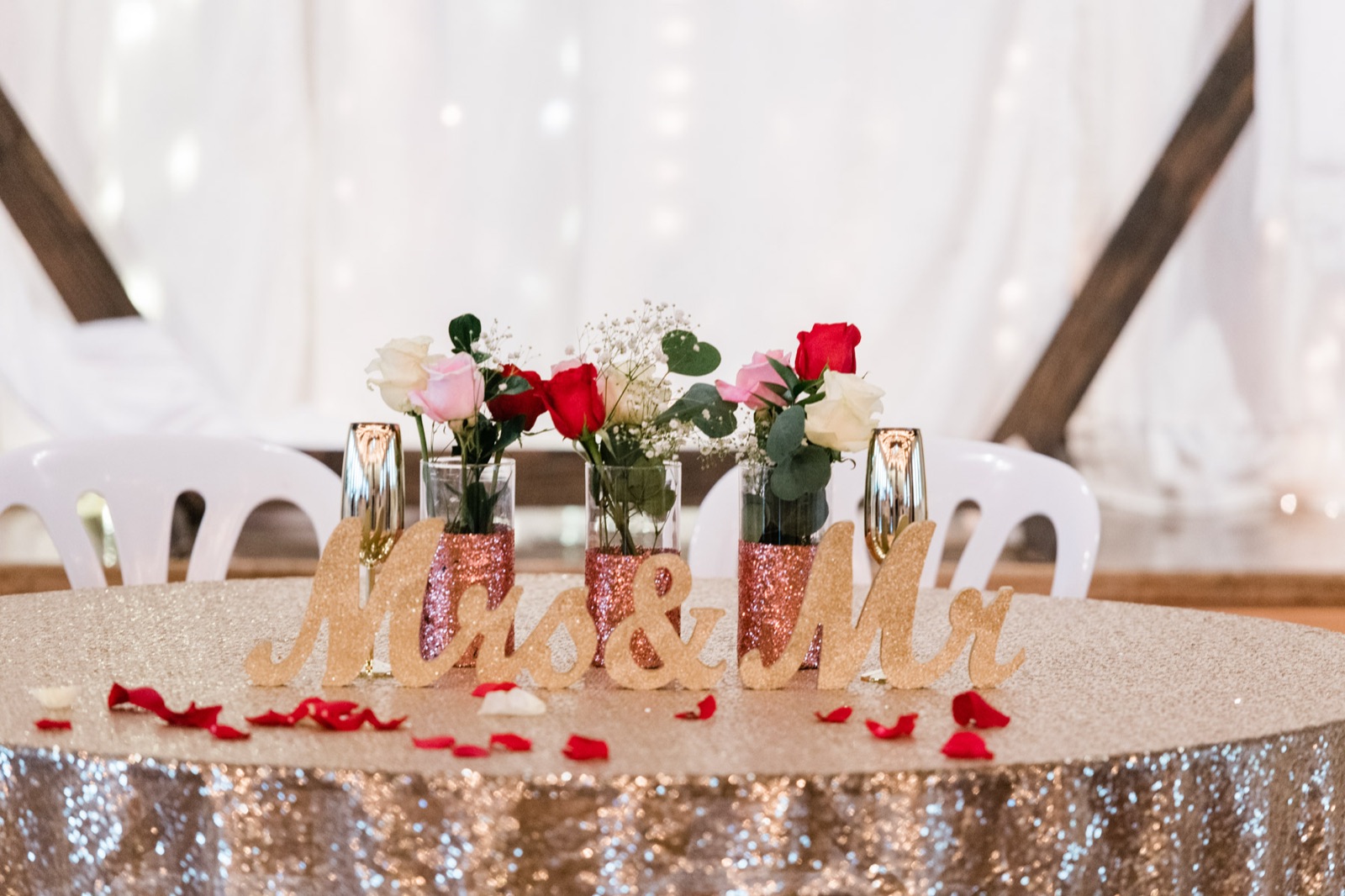 Sweetheart table with glitter Mrs and Mr letters, rose bud vases, and scattered petals at Green Villa Barn in Independence, Oregon