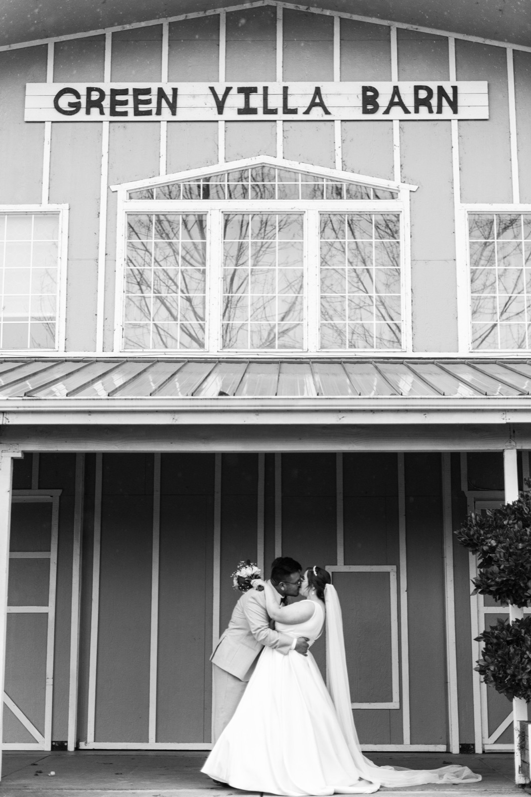 Black and white photo of a couple dip-kissing under the Green Villa Barn sign in Independence, Oregon
