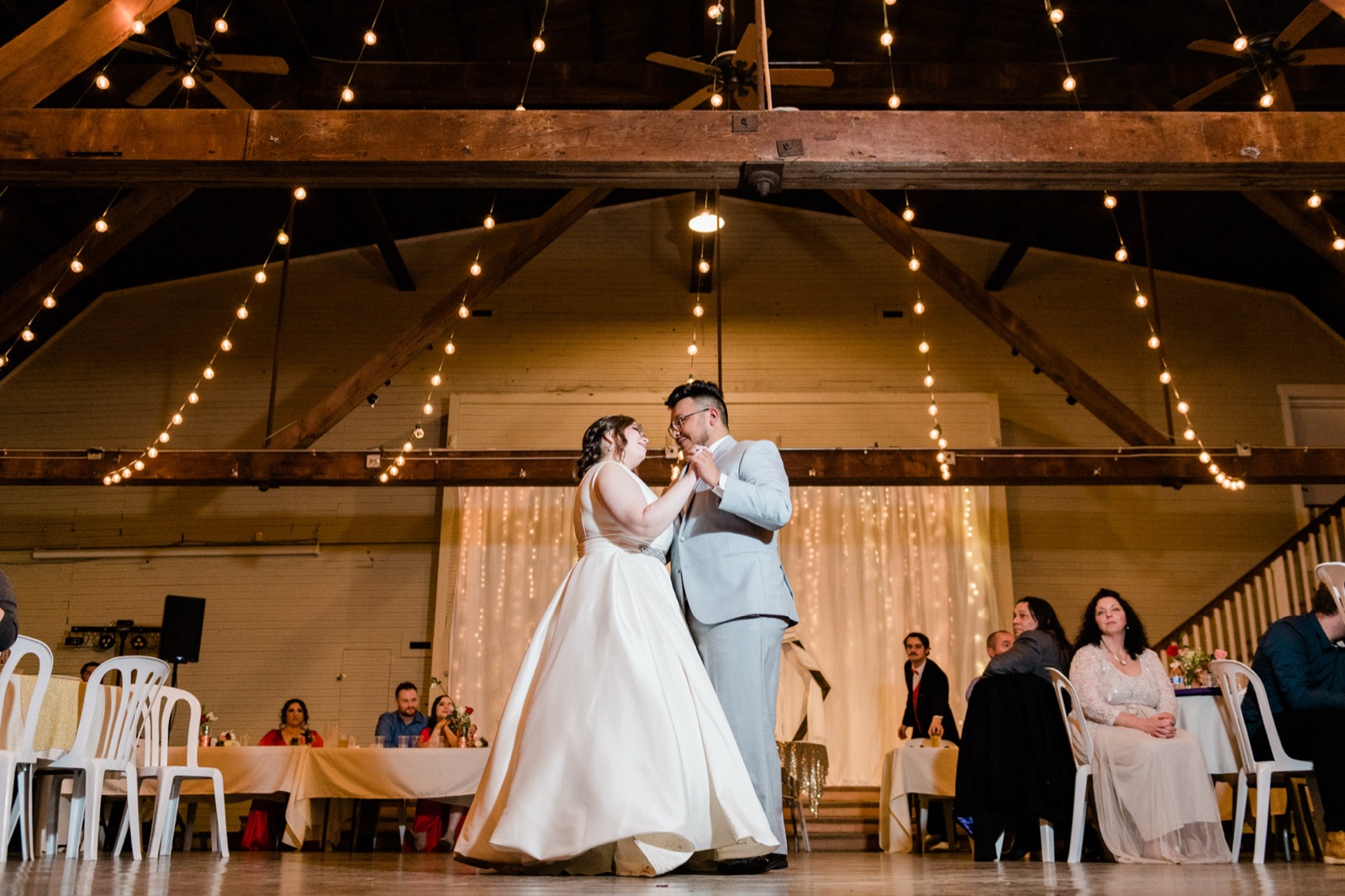 Bride and groom share a first dance under string lights and wood beams at Green Villa Barn in Independence, Oregon
