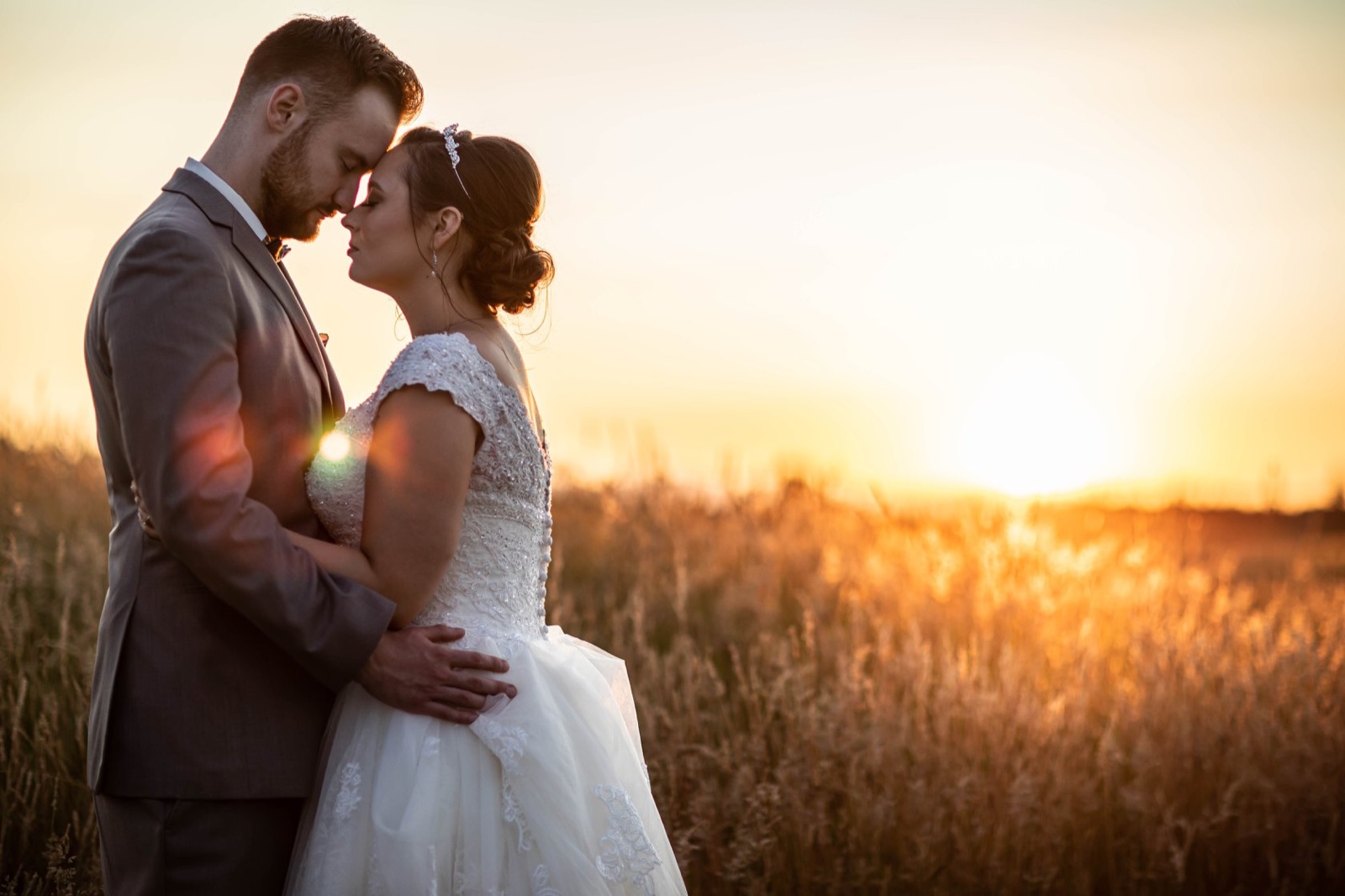 Bride and groom touch foreheads in a golden field at sunset