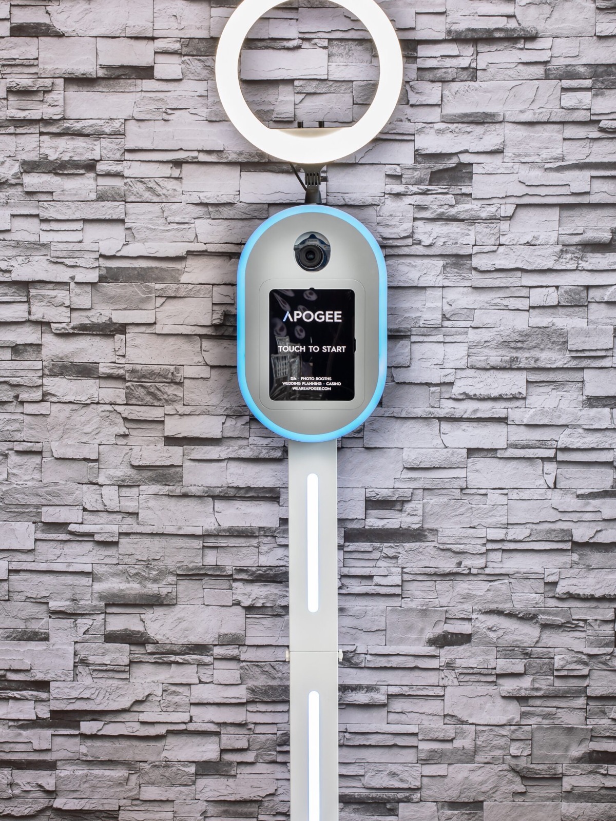 Apogee touch-screen photo booth kiosk with ring light against a gray stacked-stone wall at Cellar 54