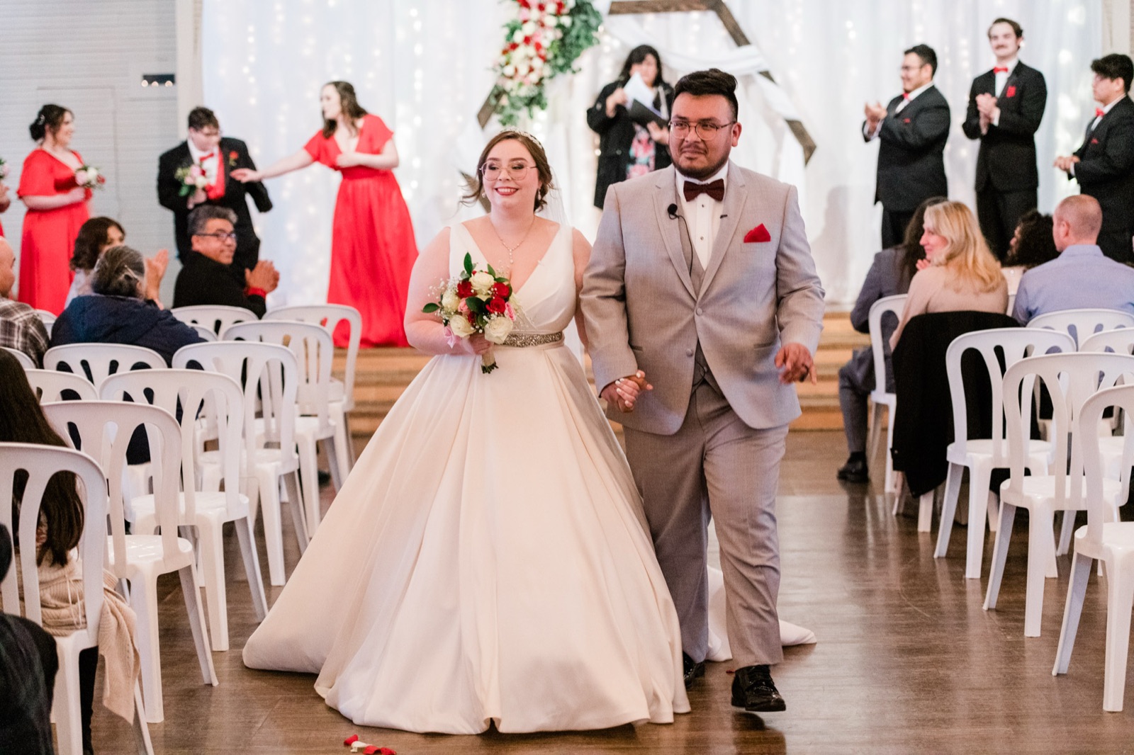 Bride and groom walk back down the aisle holding hands as guests and wedding party applaud at Green Villa Barn