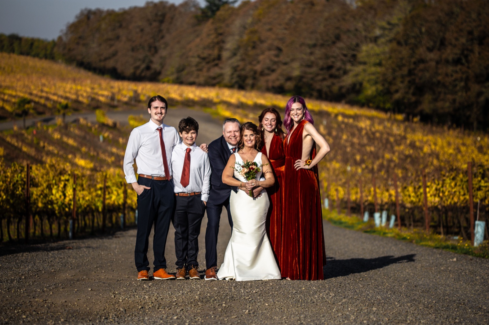 Bride and family posing on a gravel road between autumn vineyard rows
