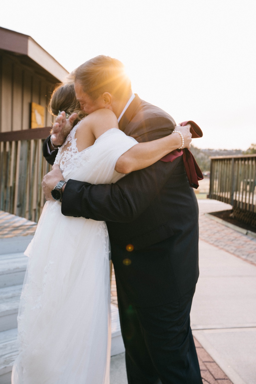 Bride in lace gown embracing in warm backlit sunset light on a wooden walkway