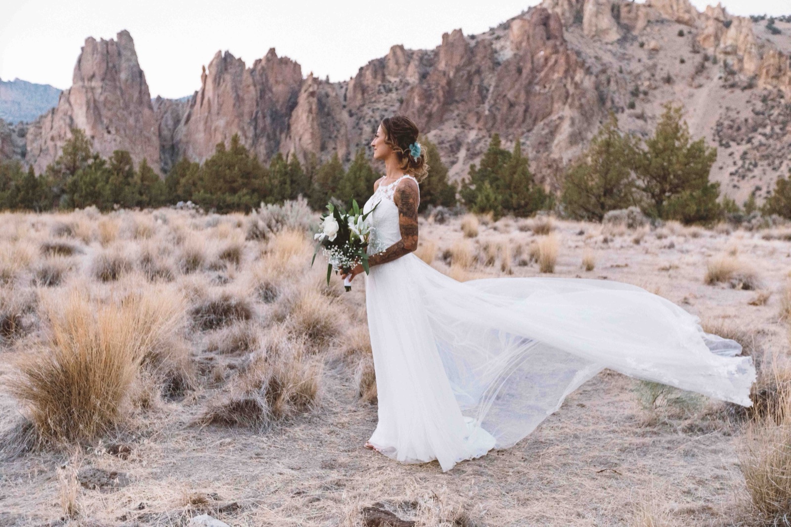 Bride in profile holding her bouquet as her tulle train blows sideways in front of desert rock spires