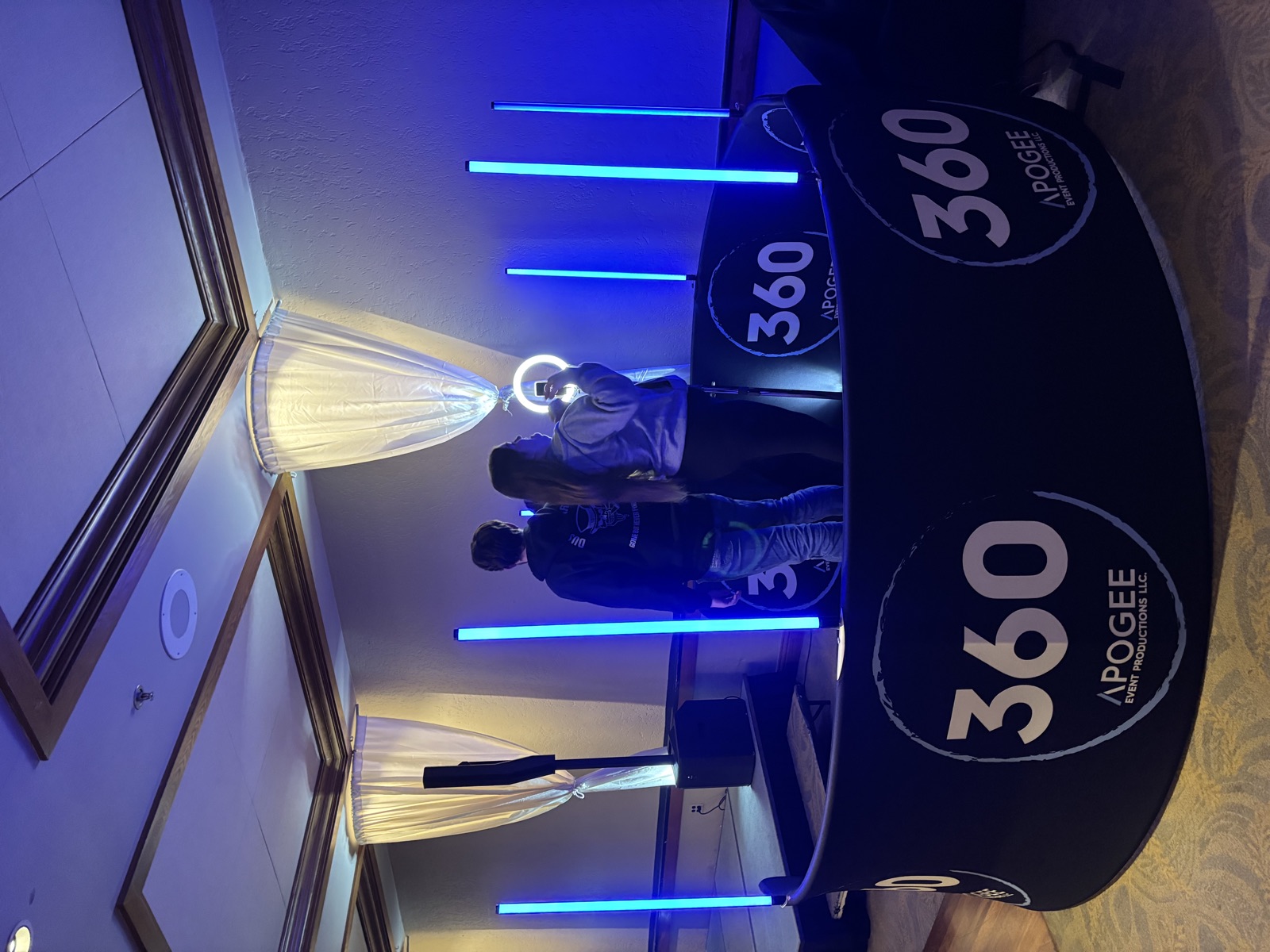 Apogee 360 booth platform with ring light, blue LED towers, and draped uplighting at an event