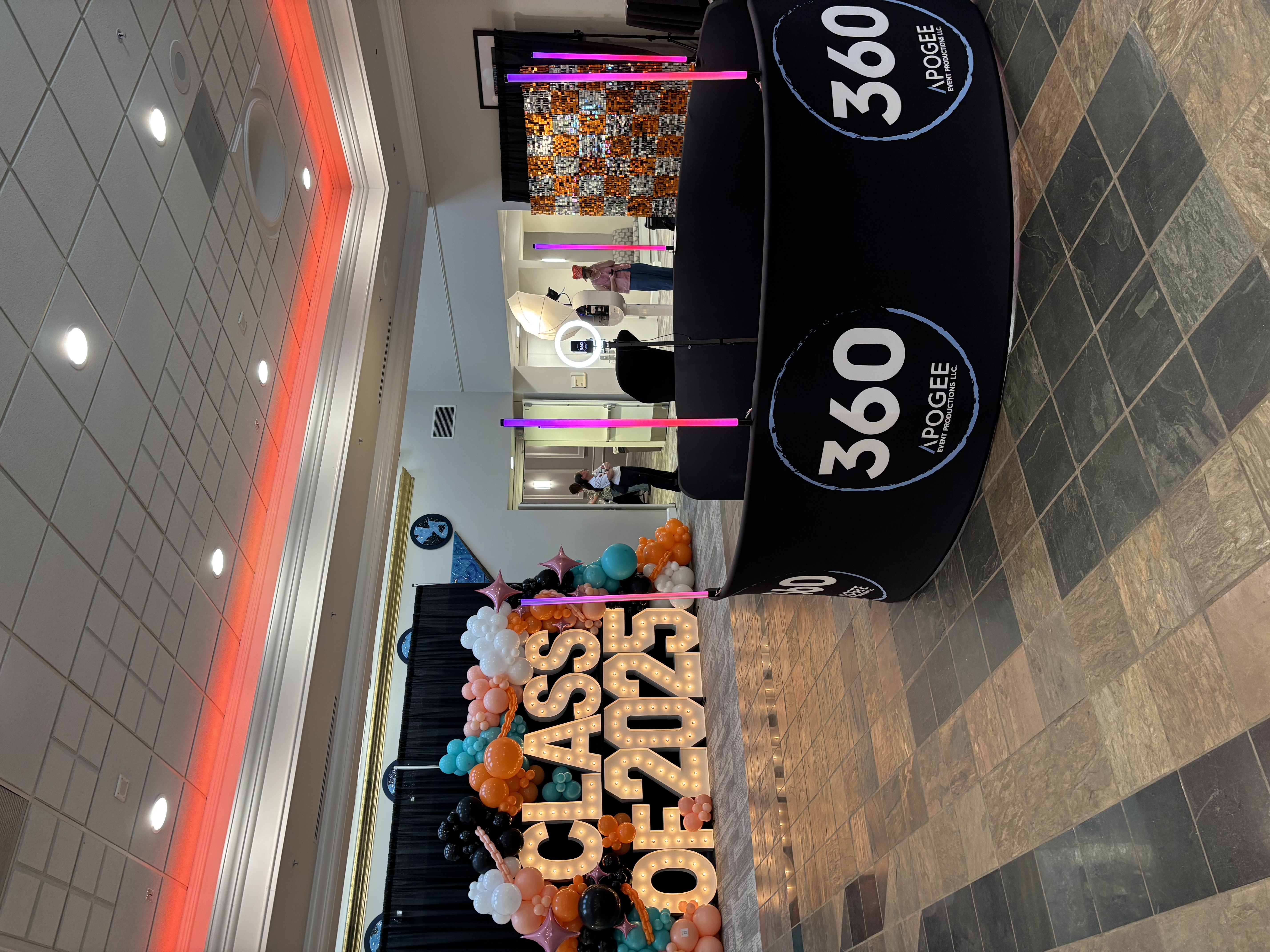 Apogee 360 photo booth enclosure set up beside a Class of 2025 balloon display and sequin backdrop