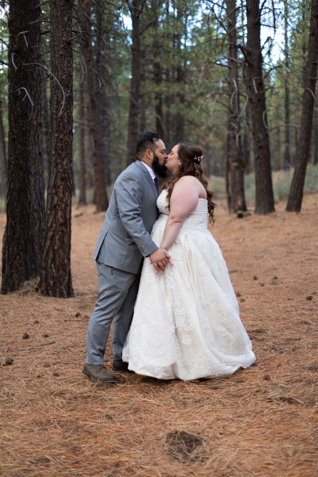 Bride and groom kiss holding hands among tall ponderosa pines
