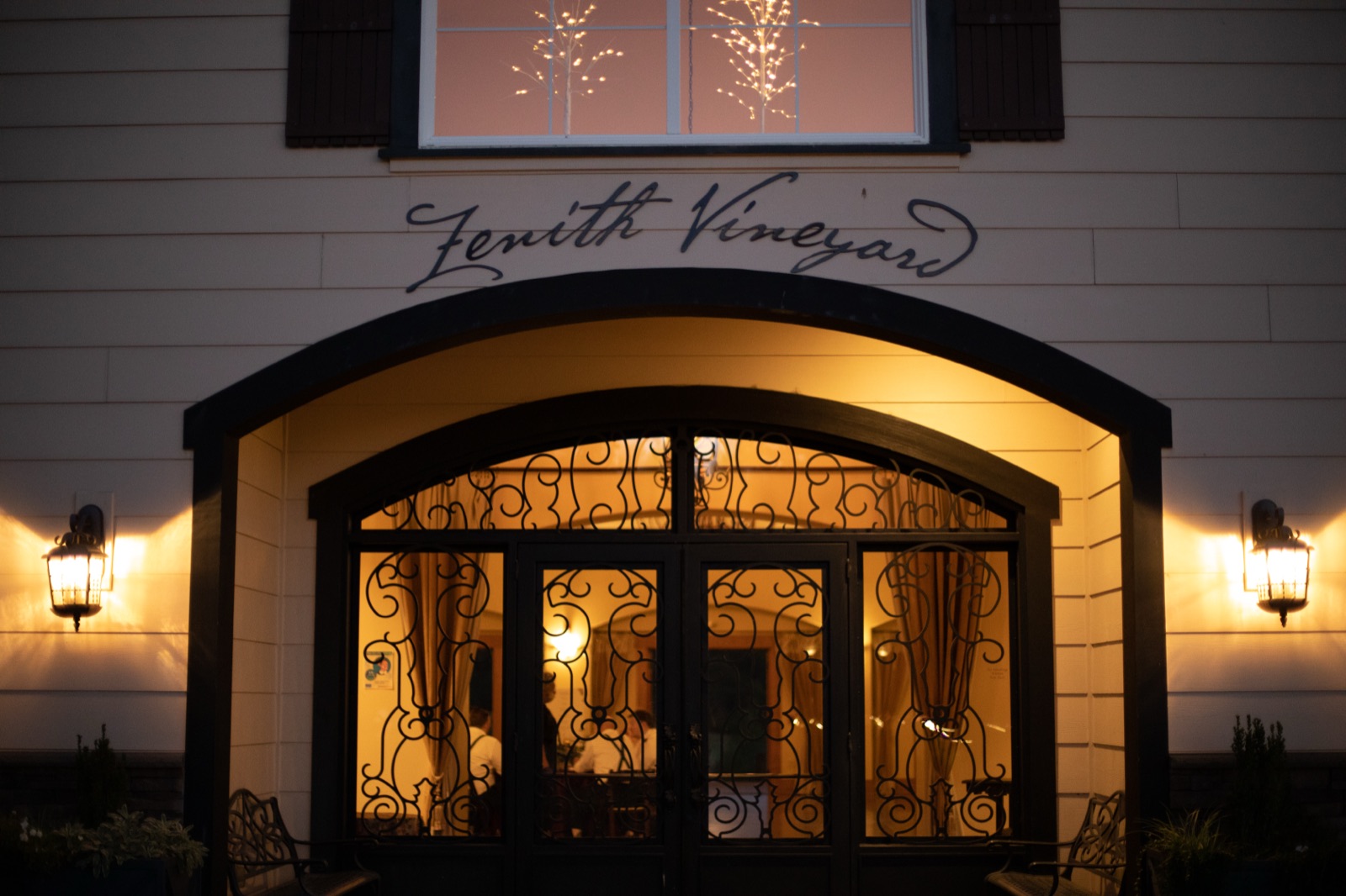 Entrance of Zenith Vineyard at dusk, warm light glowing through iron-scrolled doors