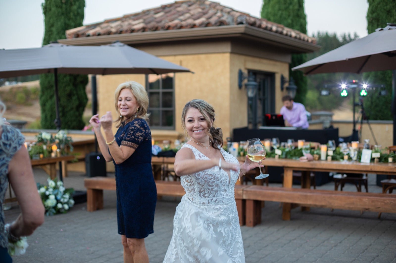Bride dancing with a wine glass on a winery patio, Apogee DJ at his booth in the background
