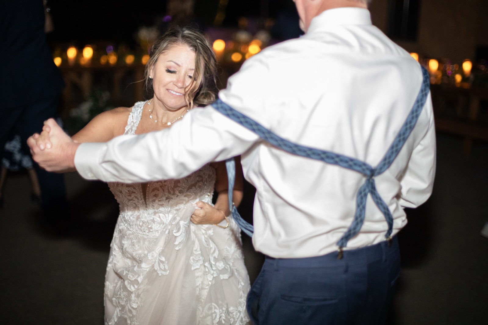 Bride dancing with a man in suspenders on a candlelit dance floor at night