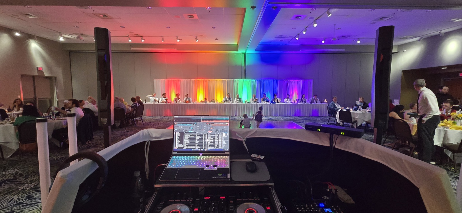View from the DJ booth of a ballroom reception in Salem, Oregon with rainbow uplighting behind the head table