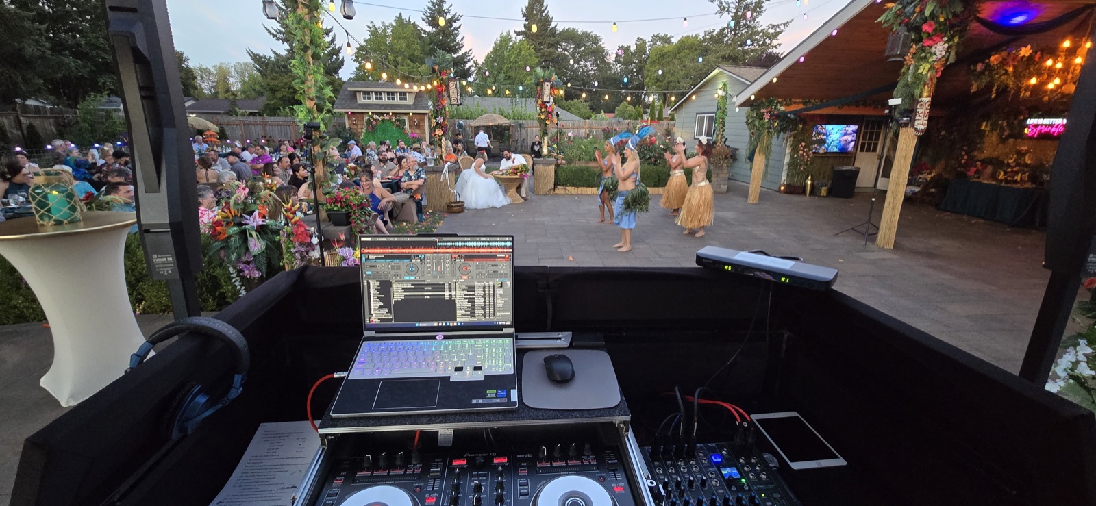 View from the DJ booth over a backyard wedding in Salem with hula dancers performing for seated guests at dusk