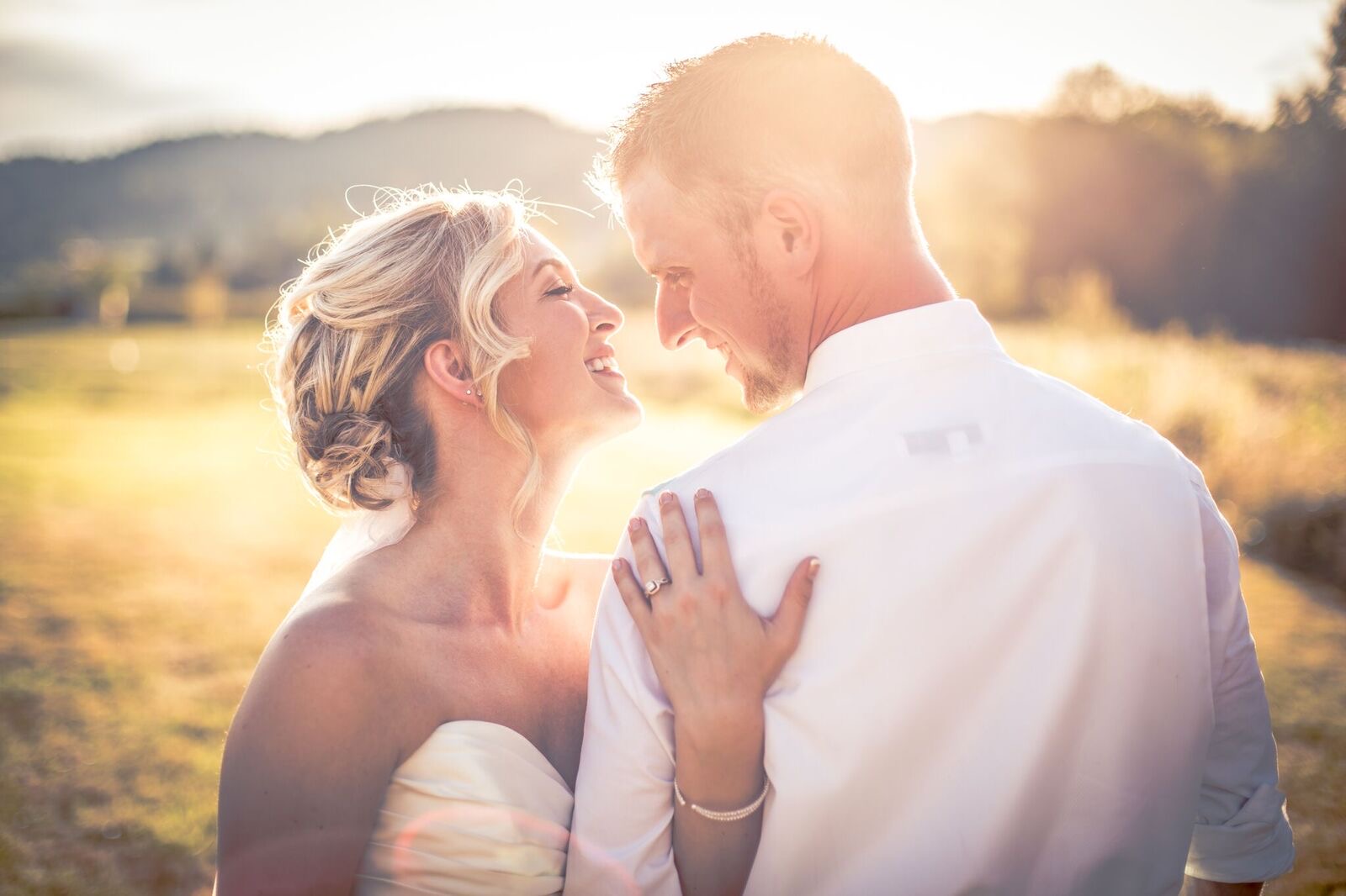 Bride and groom smile at each other in golden backlight in an open field near Salem
