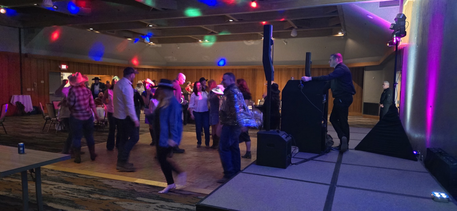 DJ Zach Thomas at his booth as guests in western wear dance under colored lights at Salishan in Lincoln City, Oregon