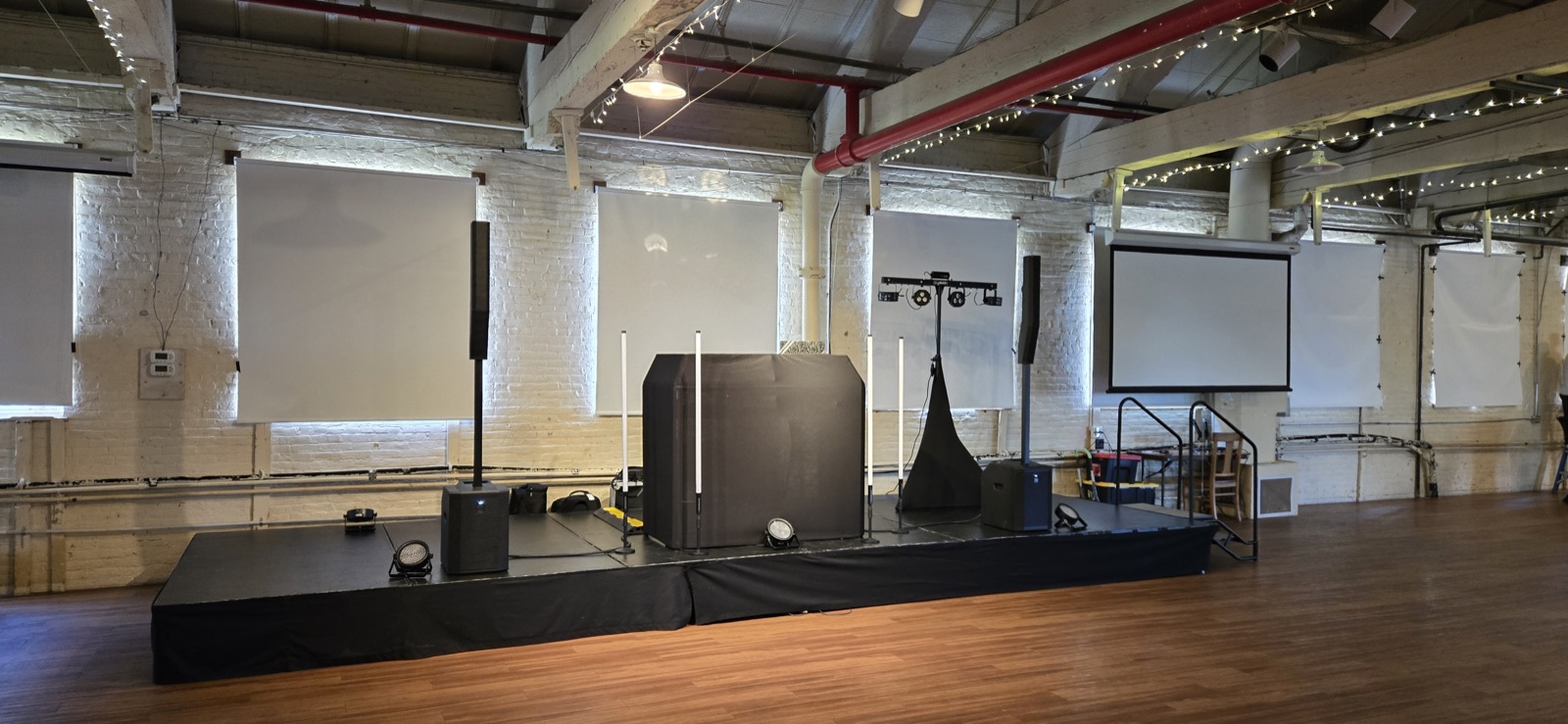 DJ stage with booth, speakers, lights, and projector screen in a brick warehouse venue