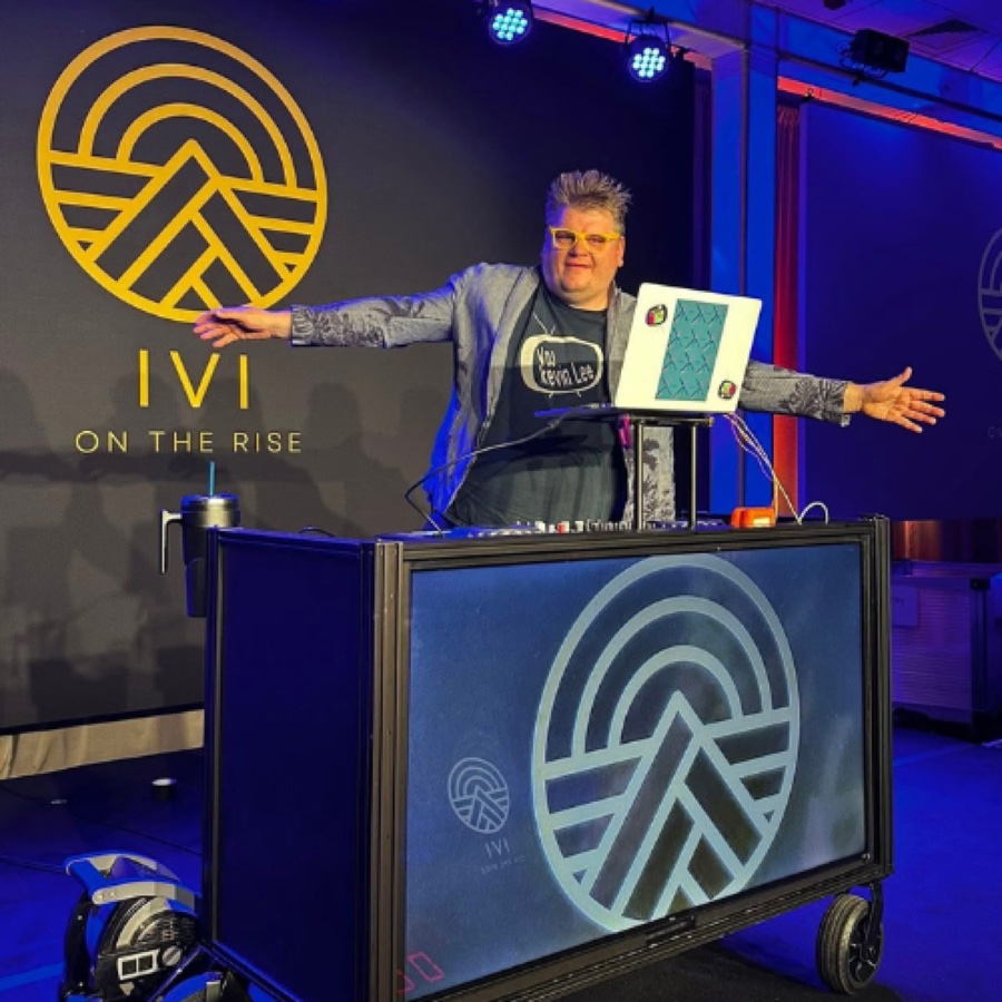 Kevin Lee with his arms out behind a DJ booth at a corporate event