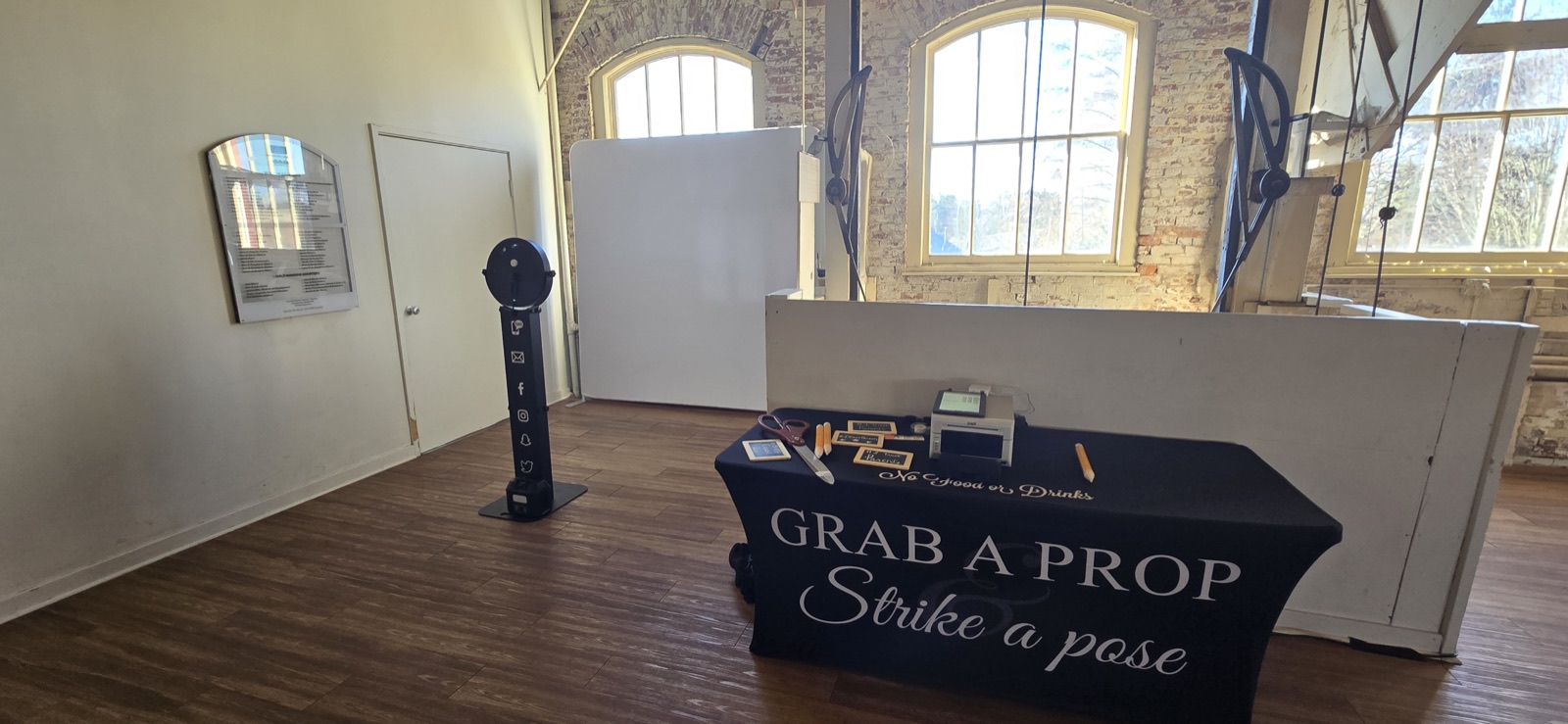 Photo booth setup with prop table, printer, and white backdrop in a brick-walled room at Willamette Heritage Center, Salem, Oregon